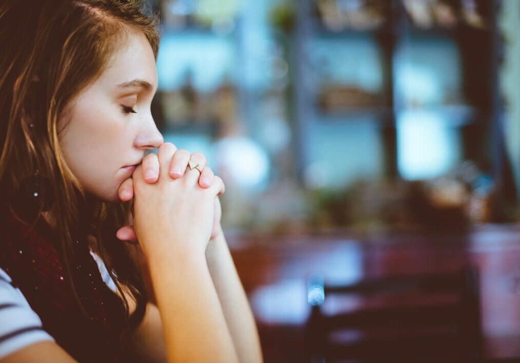 A woman sitting in front of a window with her hands clasped together.