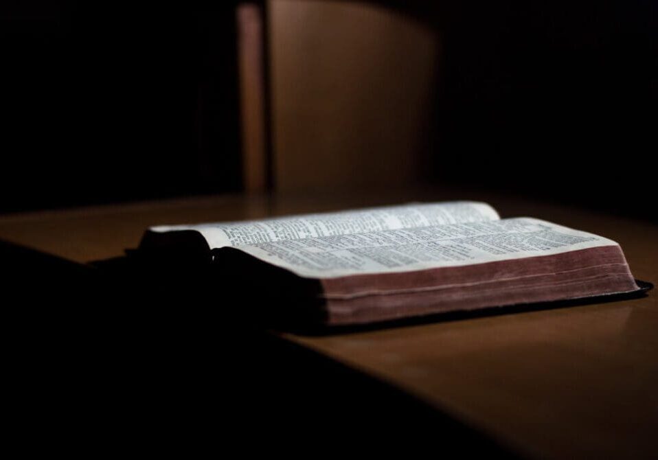 A book is open on the table in front of a window.